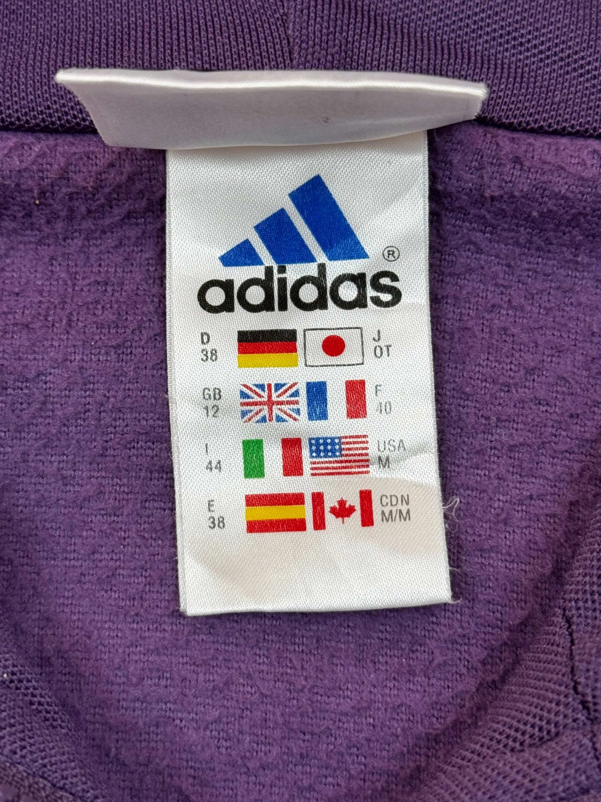 Lila Adidas Fleece in Größe M mit Pflegeetikett und Markenlogo.